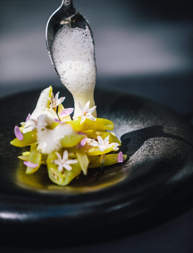 A dish at Michelin starred restaurant Vinkeles in luxury boutique hotel Royal Gate Resort leading hotels of the world on a black plate with yellow wax beans.